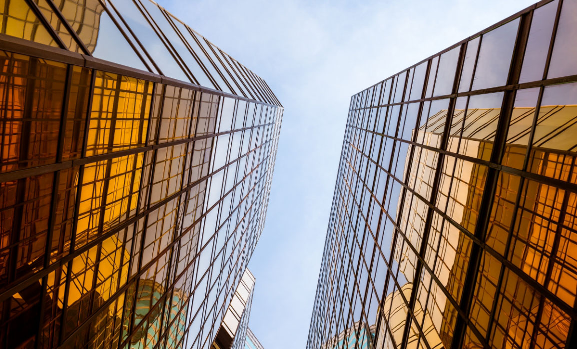 A shot of narrow blueish sky between two glassy and reflective tall buildings