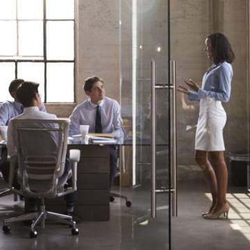 An image of a nice interior building, with a glass boardroom and people meeting in it