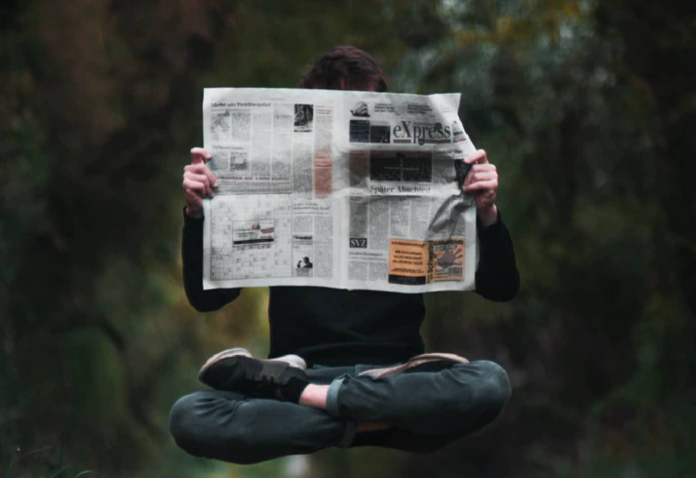 A man reading a newspaper while floating in the air with his legs crossed