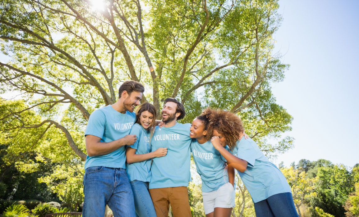 A diverse group of people wearing volunteer t-shirts, hugging and laughing with each other