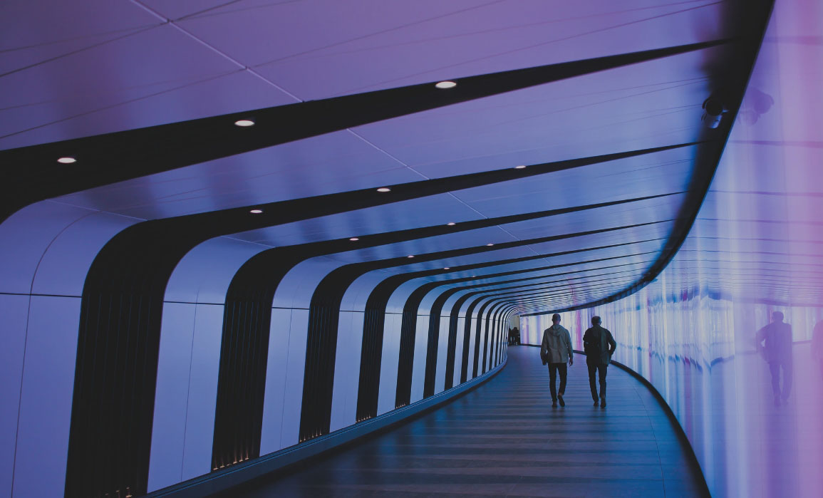 Two people walk down a curved hallway, which is tinted with a mauve color.